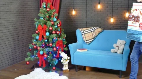 A young man arranges Christmas presents under an already dressed tree Stock Footage 82266647