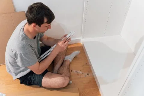 Young man assembling a cabinet sitting on the floor of his new home Stock Photos