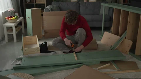 Young man assembling flat pack furniture using cordless screwdriver Stock Footage 332430935