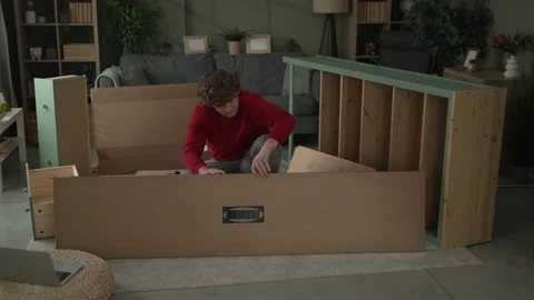 Young man assembling new wooden furniture in living room Stock Footage 332430854