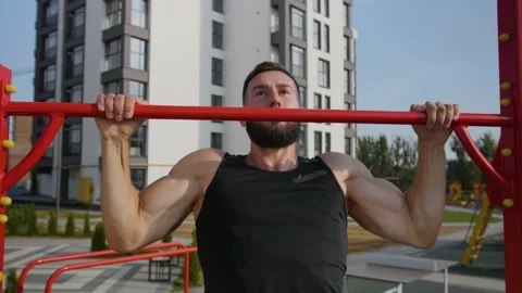 A young man of athletic build pulls up on a red horizontal bar. Video stock 140105992