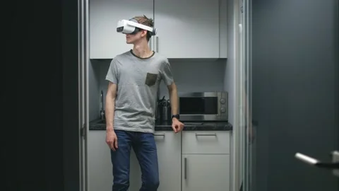 Young man in augmented reality goggles stand in small kitchen at home or in Stock Footage 194708694