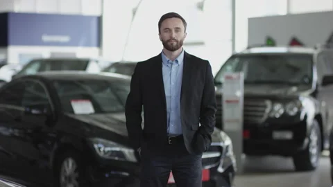 A young man in the auto dealership is posing. He is standing between new cars Stock Footage 130284653