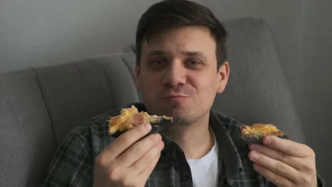 Young man bachelor sitting on sofa at home and eating two slices of tasty pizza. Stock Footage 153093573