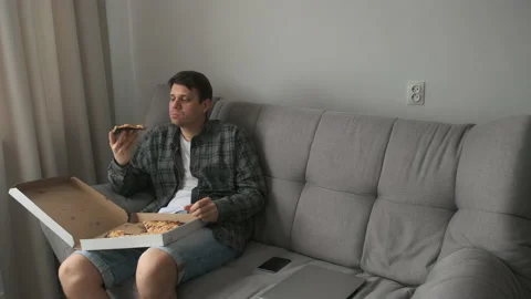 Young man bachelor sitting on sofa at home and eating tasty pizza from delivery. Stock Footage 158803809