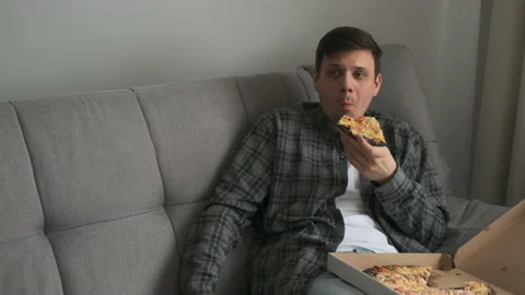 Young man bachelor sitting on sofa at home and eating tasty pizza from delivery. Stock-Footage 159488419