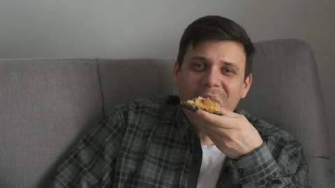 Young man bachelor sitting on sofa at home and eating tasty pizza from delivery. Video stock 159743398