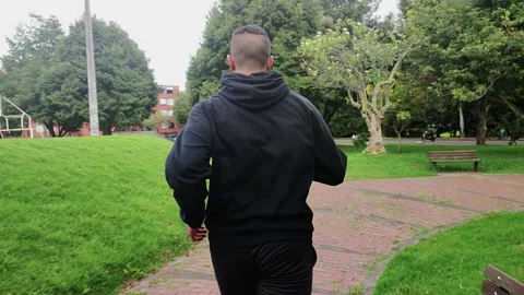Young man from the back running in a forest of a park in the city Stock Footage 248310673
