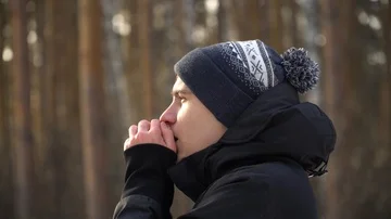 A young man on the background of the forest warms his hands with breath in Stock Footage 85672415