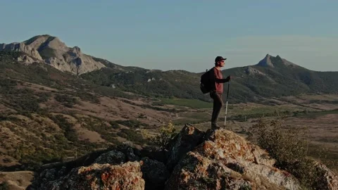 Young Man with a Backpack and Nordic Walking Sticks Stands on the Top of a Mount Stock Footage 150590979
