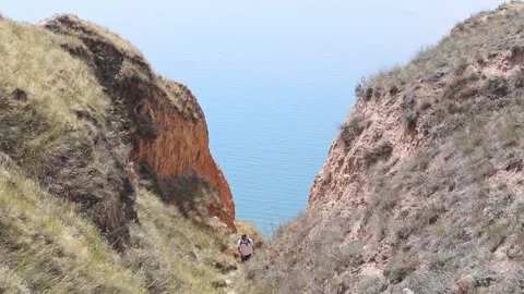 Young man with backpack climbing up by trail from beach Stock Footage 146752079