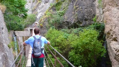 Young man with backpack crossing hanging bridge Stock Footage 82472061