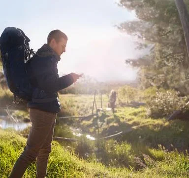Young man with backpack hiking, checking smart phone in sunny field 스톡 사진