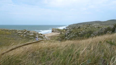 A young man with a backpack on his shoulders walks along the shore near the sea. Video stock 99372290