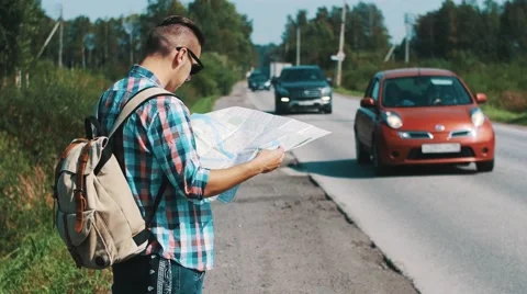 Young man with backpack hitchhiking at road in countryside. Map. Thumbing up Stock Footage 67413223