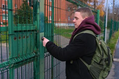 Young man with backpack opening aged green metal gate, accessing a secure a.. Stock Photos