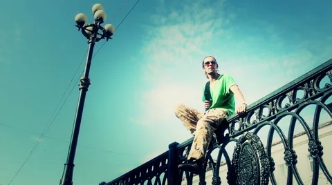 A young man with a backpack sitting on the fence of the bridge Stock Footage 40310479