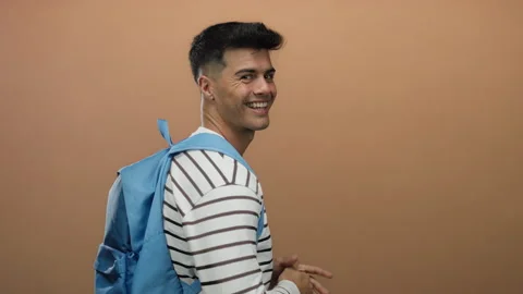 Young man with backpack smiling and giving thumbs up against an isolated br.. Stock Footage 313462934
