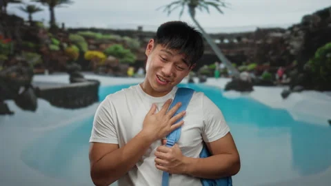 Young man with backpack smiling warmly at luxury outdoor pool in resort set.. Stock Footage 311500173