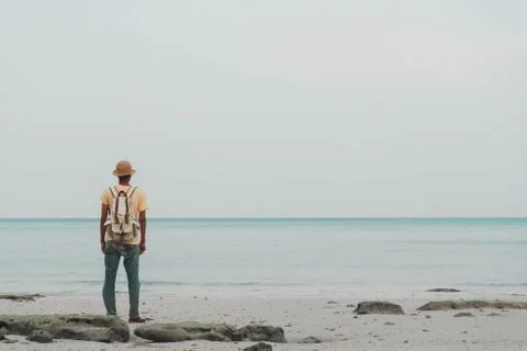 Young man with backpack standing on beach and looking to horizon of ocean. co Stock Photos