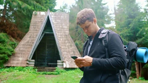 Young man with a backpack stands in the forest and writes a message on the phone Stockbeeldmateriaal 198502970