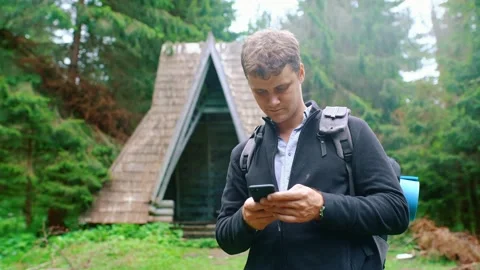 Young man with a backpack stands in the forest and writes a message on the phone Stock Footage 198503191