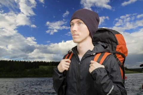 Young man with a backpack stands in front of a river. Stock Photos