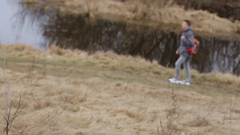 Young man with backpack walking along river Stock Footage 128573144