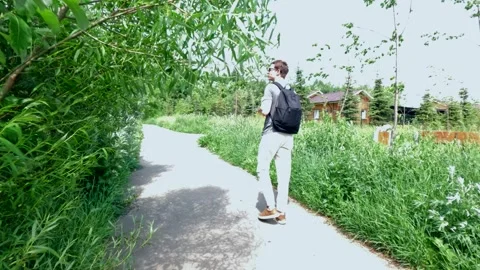 A young man with a backpack is walking along the road to the village house Stock Footage 277590844