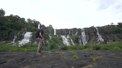 Young man with backpack walking in nature with amazing waterfall in background. Stock Footage 144084742