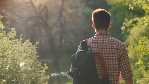 Young man with backpack walking by river in nature during golden hour sunli.. Stock Footage 334592843