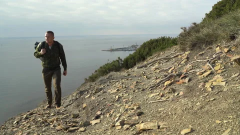 A young man with a backpack walks along the mountainside Stockbeeldmateriaal 143411503