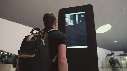 Young man with backpack is watching electronic timetable in airport hall Stock Footage 96297981