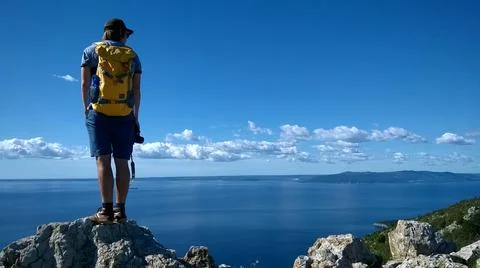 Young man with backpack watching over view with ocean Stock Photos