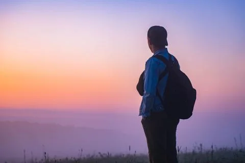 Young man with a backpack watching the sunrise on nature. male tourist hiker  Stock Photos