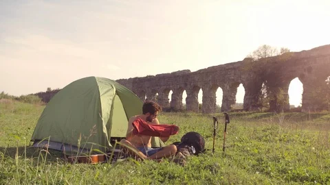 Young man backpacker dressing wearing t-shirt outside camping tent sitting on Stock-Footage 86269906
