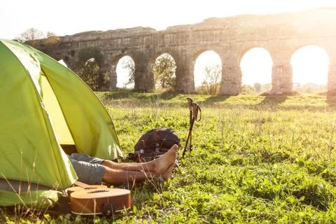 Young man backpacker sleeping in camping tent on grass with feet outside in Stock Photos