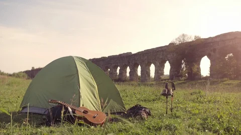 Young man backpacker wakes up exits camping tent in front of roman aqueduct Stock-Footage 86273147