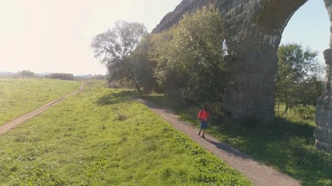 Young man backpacker walking on dirt road along ancient roman aqueduct in orange 스톡 동영상 90342109
