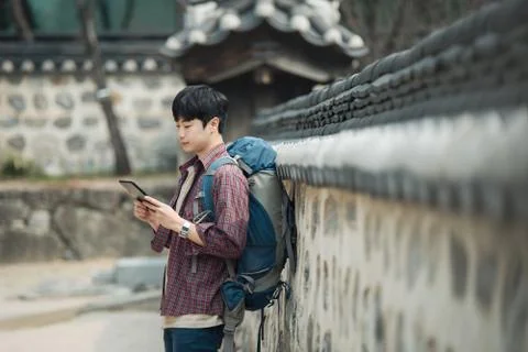 A young man backpacking in Korea. Using a tablet computer leaning against a w Stock Photos