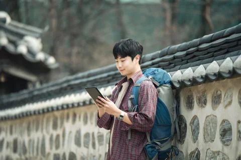A young man backpacking in Korea. Using a tablet computer leaning against a w Stock Photos