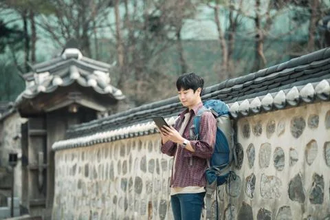 A young man backpacking in Korea. Using a tablet computer leaning against a w Stock Photos