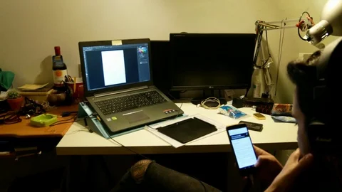 A young man from back,uses a smartphone at a desk with a notebook on Stock Footage 102231483