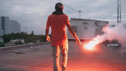 Young man in balaclava with red burning signal flare on the roof with graffiti Stock Footage