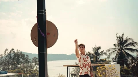 Young man on the balcony playing darts in tropical paradise with palm trees in Stock-Footage 334672221