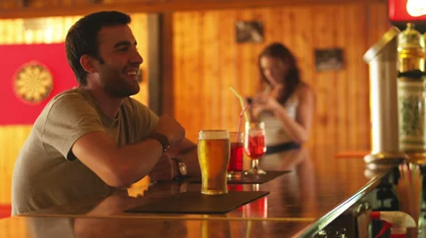 A young man at the the bar with a beer, talking with a bartender out of frame Video stock 33847560