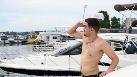 A young man with a bare torso in jeans stands on a boat, looks into the distance Vidéo 91996289