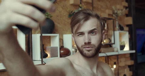 A young man with a bare torso takes pictures with his phone in the kitchen. Stock Footage 144610744