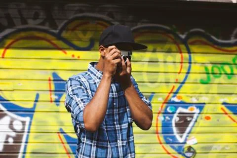 Young man with baseball cap and camera taking photos in front of roller shutter Stock Photos