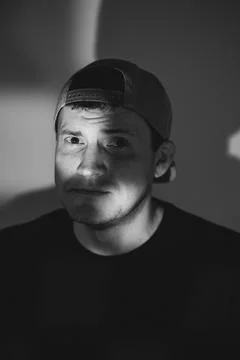 Young man in a baseball cap posing for a portrait. Dramatic lighting with s.. Stock Photos